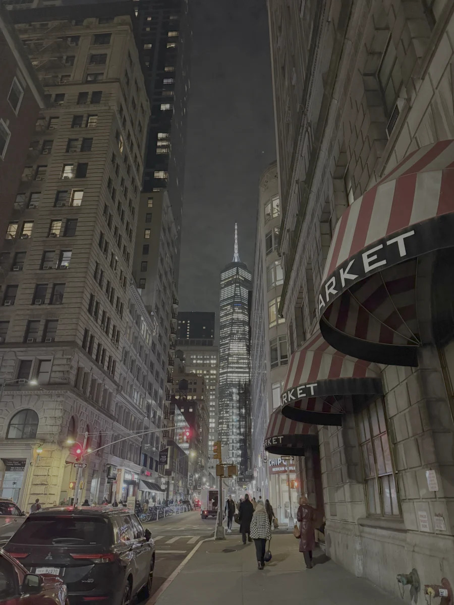 A nighttime New York City street with One World Trade Center in the distance